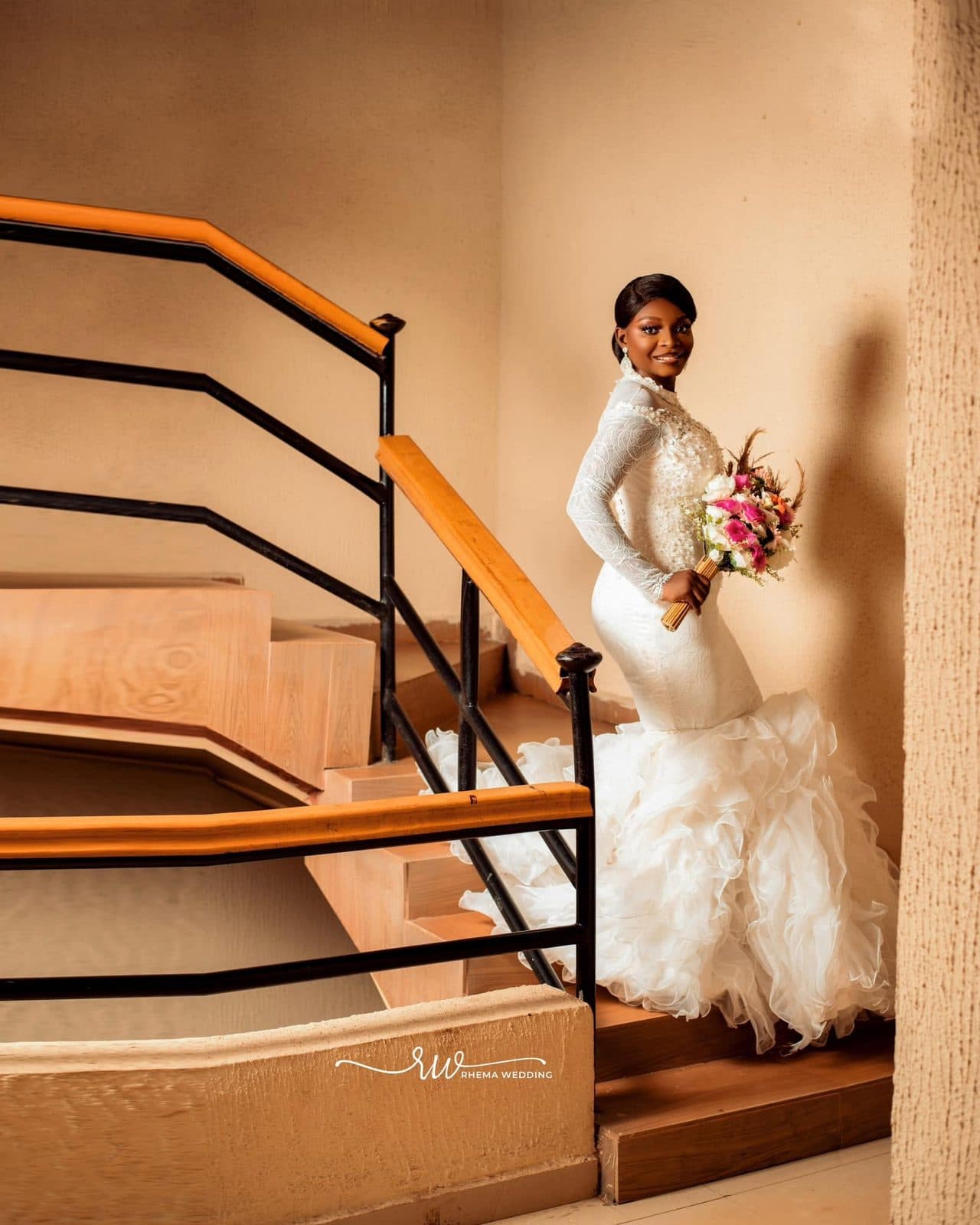 A bride in a long-sleeved mermaid gown on a staircase
